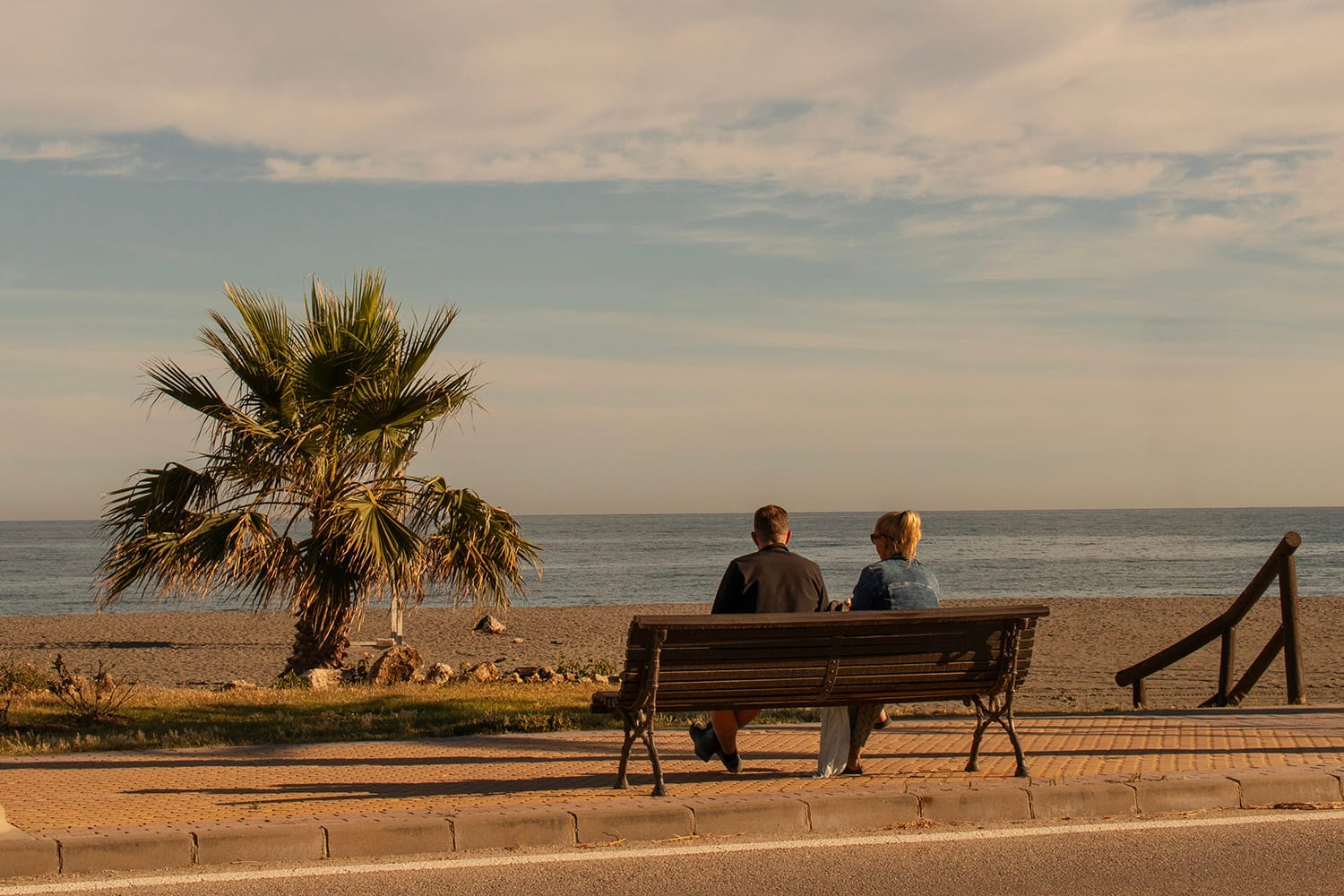 A couple relaxes on a bench looking across the beach at the sea as the evening sun goes down at Benajarafe. Photo by Jason Elliott for the eastofmalaga.com website.