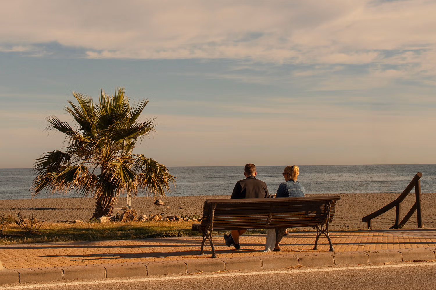 A couple relaxes on a bench looking across the beach at the sea as the evening sun goes down at Benajarafe. Photo by Jason Elliott for the eastofmalaga.com website.